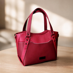 Red structured handbag with twin handles and a front zip pocket, displayed on a wooden table