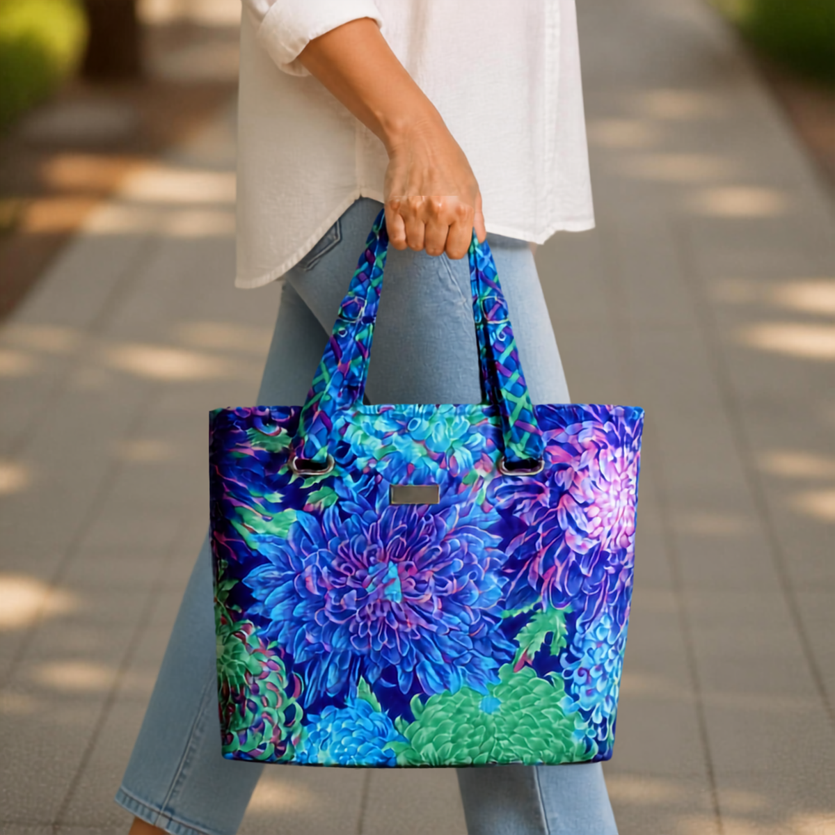 A person carrying a vibrant blue floral tote bag with green and purple flowers.