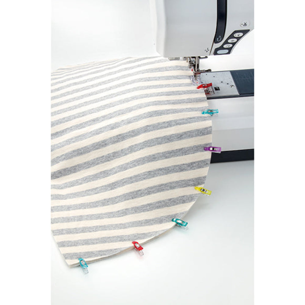 Striped fabric being sewn on a sewing machine with pins holding the edges together.