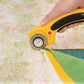 Yellow rotary cutter being used on fabric with a green cutting mat underneath