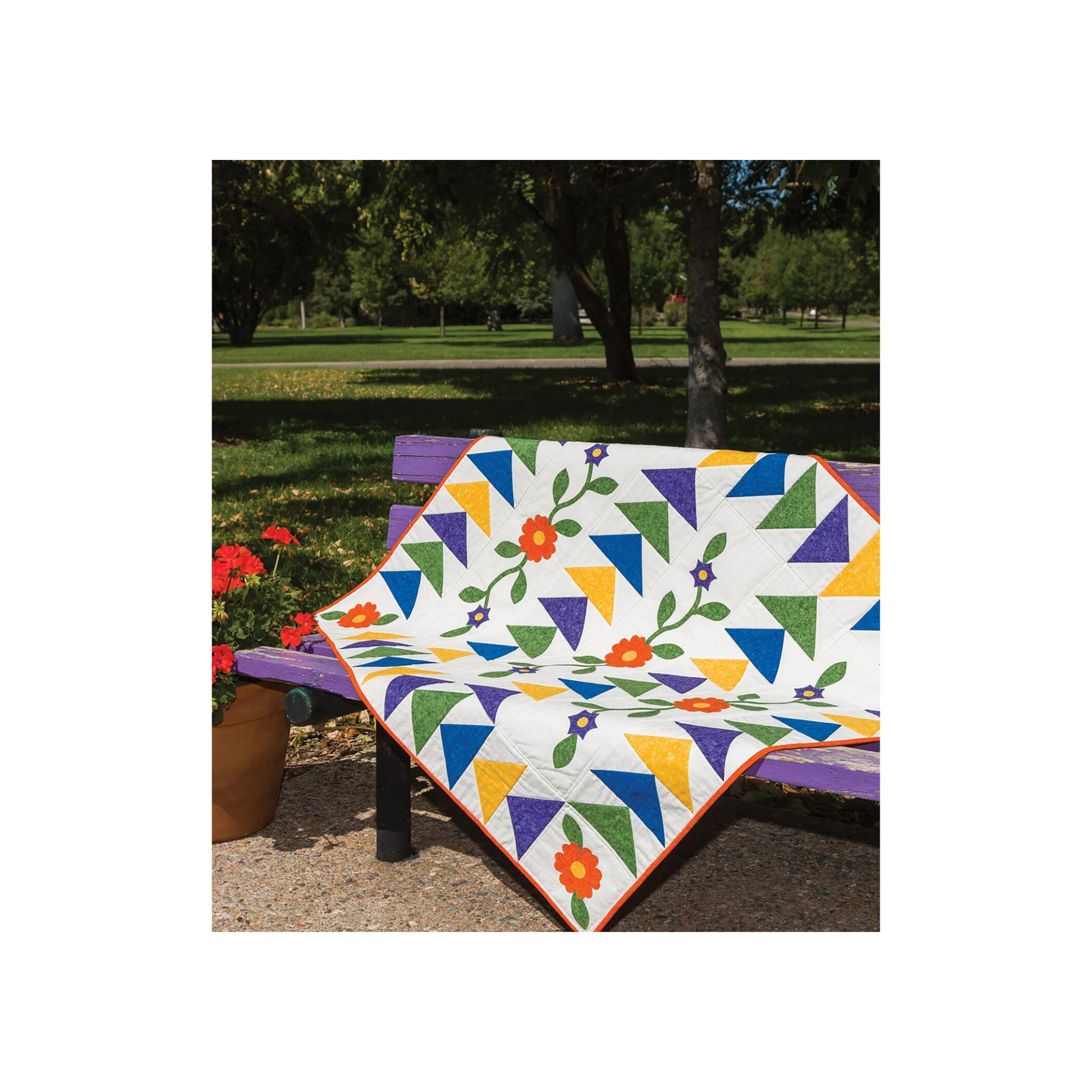 AccuQuilt GO! Round Flower quilt draped outdoors on a bench with red geraniums and triangle patchwork