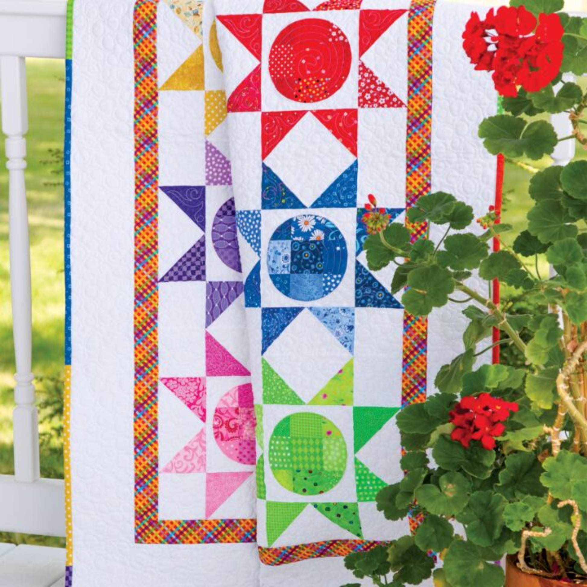 AccuQuilt GO! Circle rainbow quilt draped over a porch chair outdoors with red geraniums