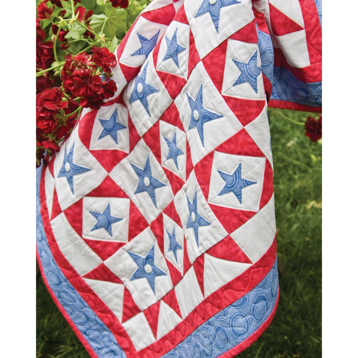 AccuQuilt GO! Star quilt draped outdoors with red geraniums and blue star blocks