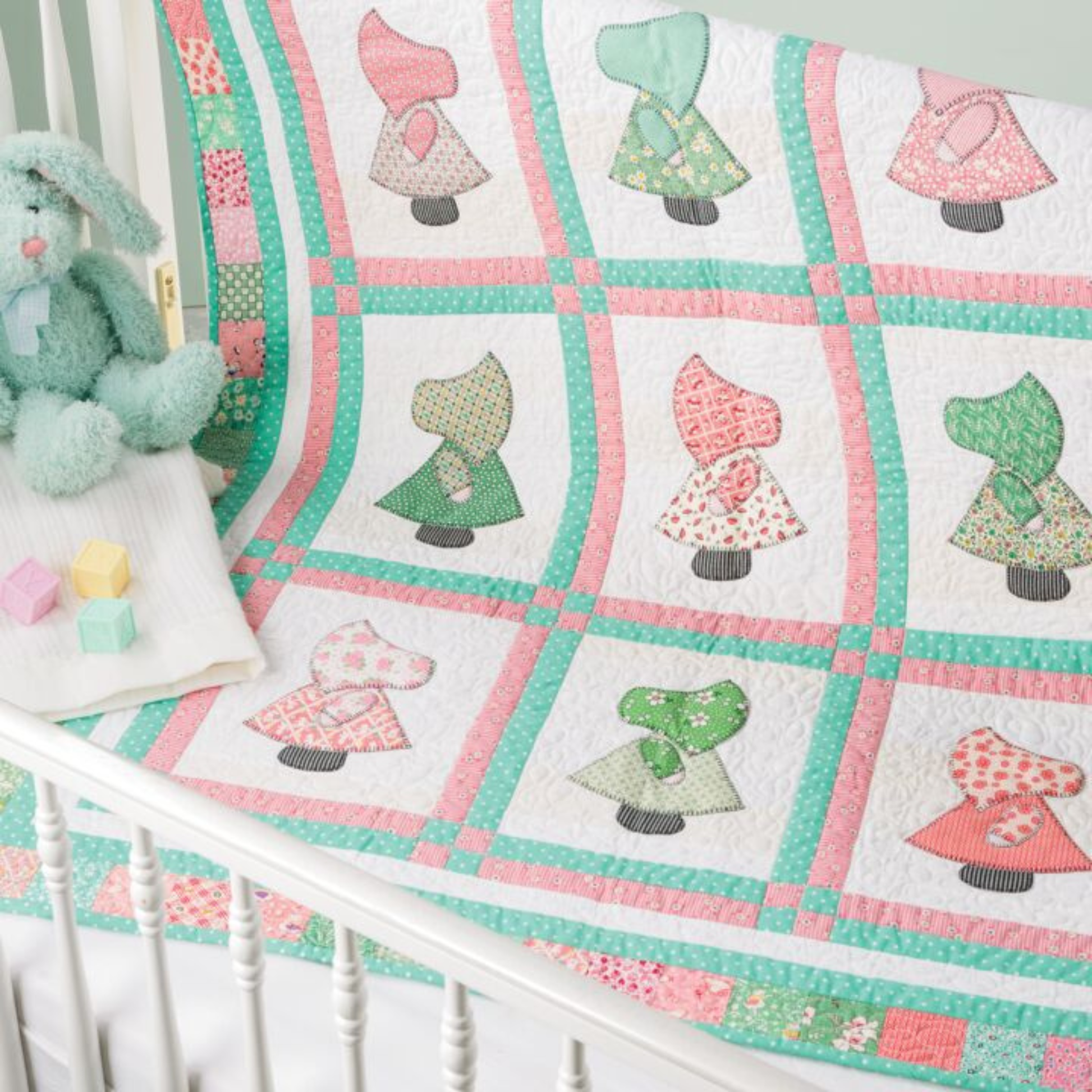 AccuQuilt GO! Sunbonnet Sue quilt draped on a white crib rail with a plush bunny toy and blocks