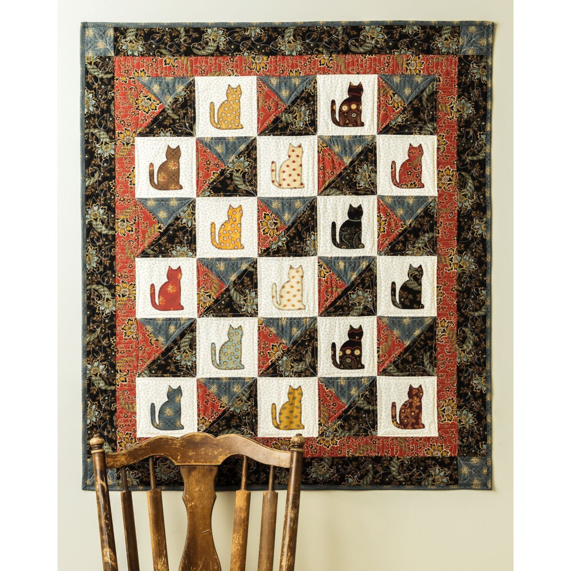 AccuQuilt GO! Calico Cat wall hanging with 20 cats in different fabrics, hung above an antique chair
