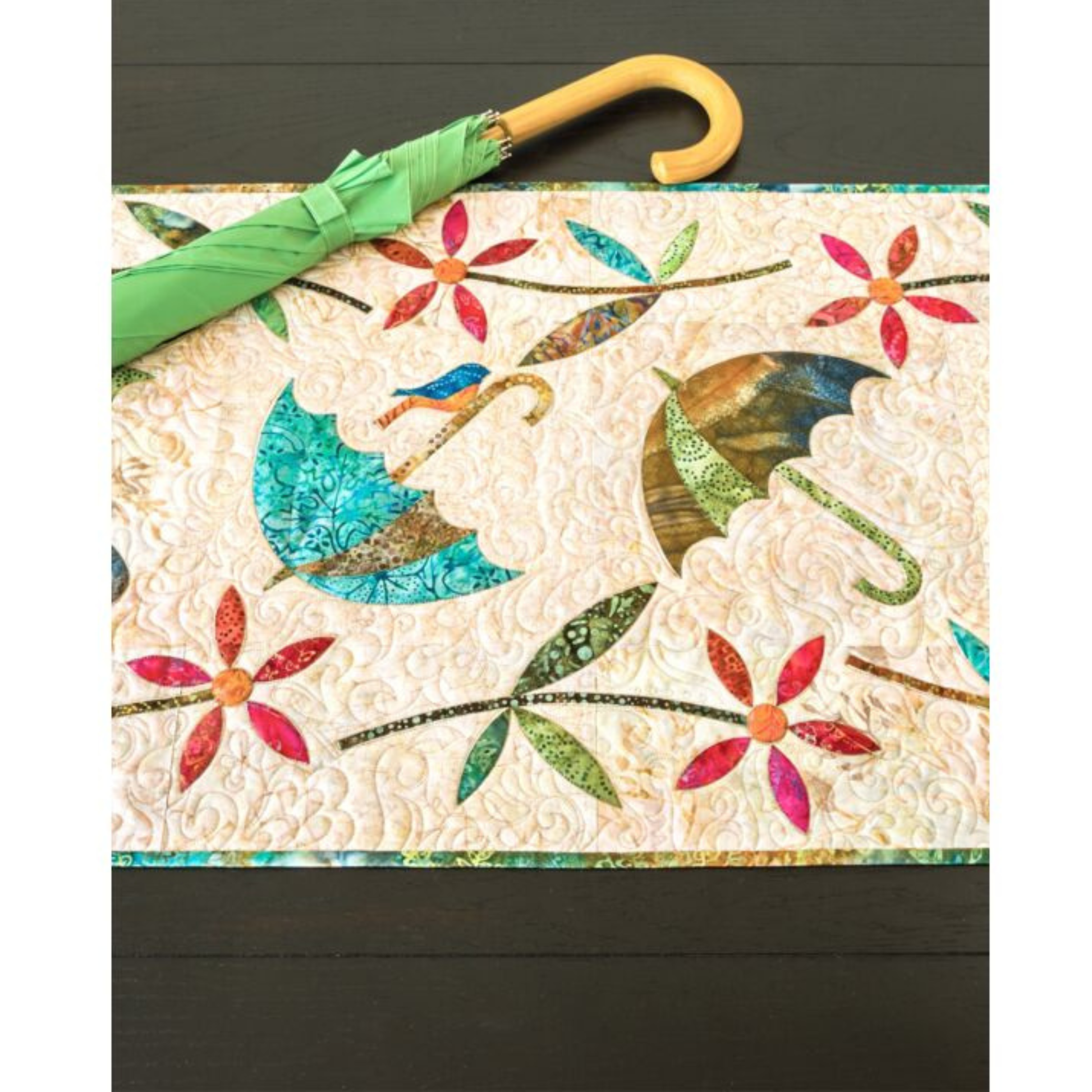 AccuQuilt GO! Dancing Umbrella table runner styled on a dark table with a real green umbrella