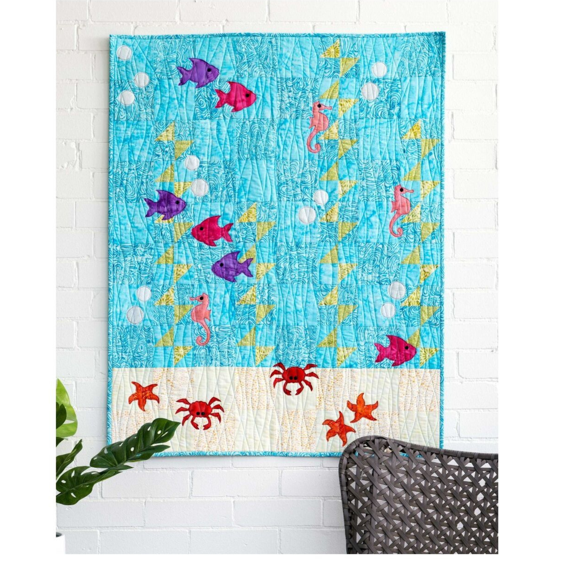 AccuQuilt GO! Sea Life Medley underwater scene quilt hung on a white brick wall with a chair