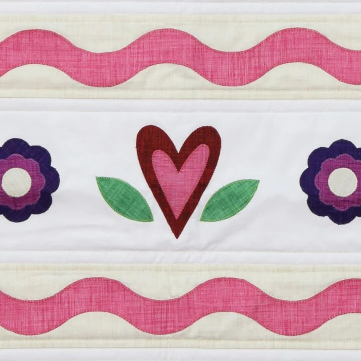 AccuQuilt GO! Queen of Hearts layered heart with leaves and flowers between pink ribbon rows