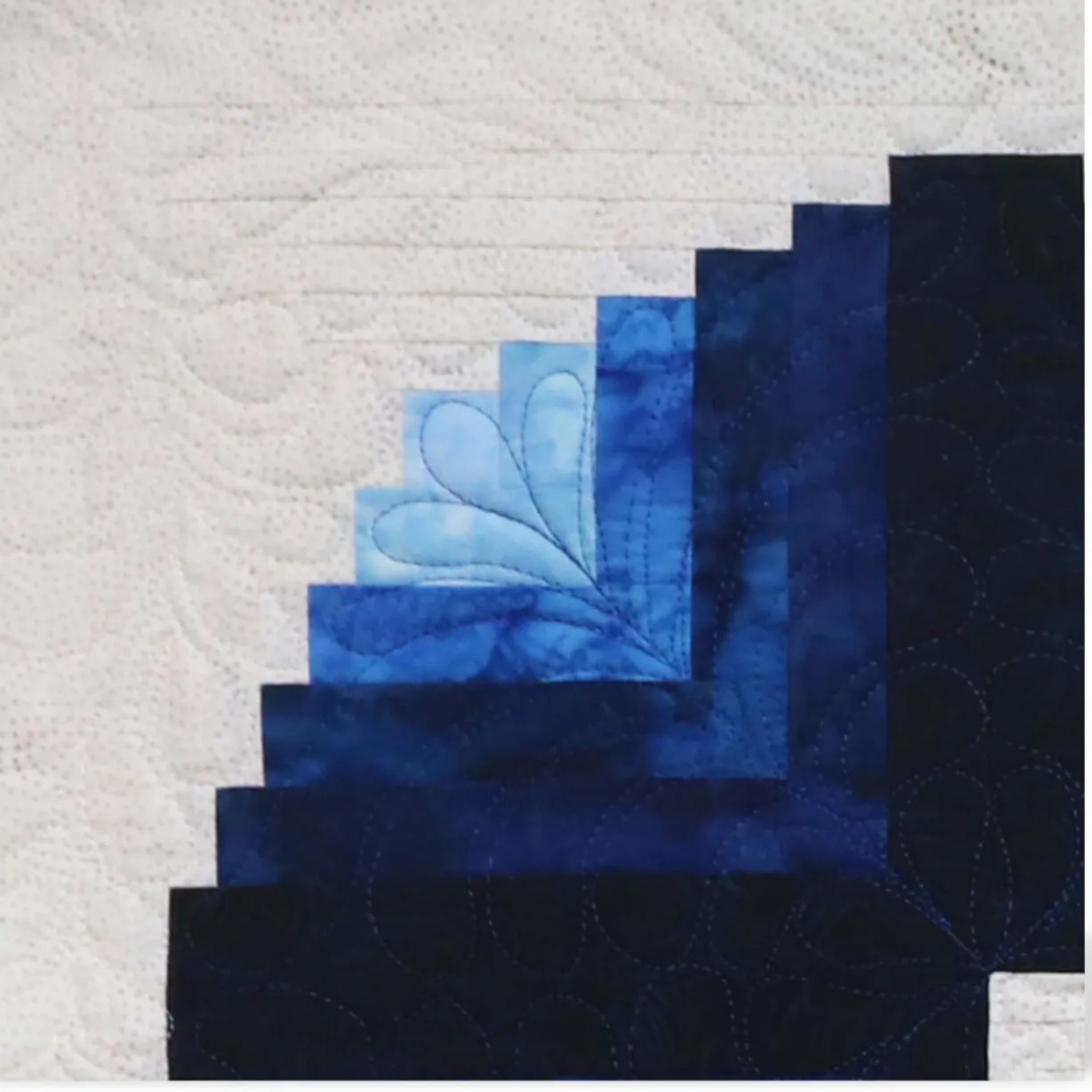 ie - close-up of curved log cabin block corner in navy and sky blue batik fabrics with feather quilting detail