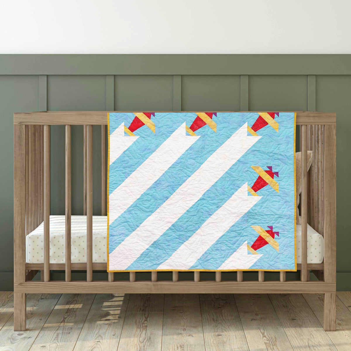 Pale blue and white baby quilt with red and yellow Airplane blocks draped over a wooden cot