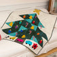 Christmas tree quilt draped over a white sofa, featuring AccuQuilt GO! Jolly Medley appliqué shapes including colourful bells, light bulbs and candy canes on teal and dark green batik, with toy cars and a train border at the base