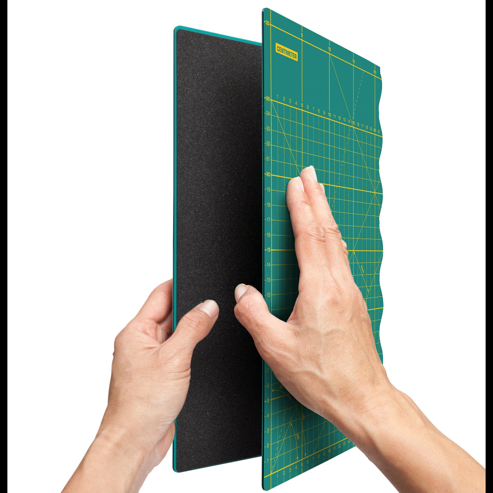 Hands holding a green cutting mat with grid lines on a white background