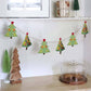 Garland of six decorated fabric Christmas trees made with the AccuQuilt GO! Tinsel die by Sue Spargo, hanging beneath white kitchen cabinets.
