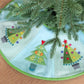 Pastel tree skirt with colourful Christmas tree appliqués made using the AccuQuilt GO! Tinsel die by Sue Spargo, displayed beneath a Christmas tree.