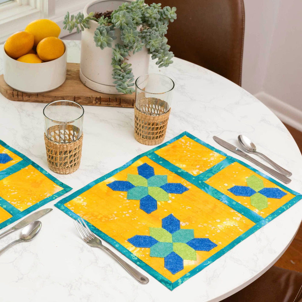 AccuQuilt GO! English Paper Piecing Honeycomb die used to make yellow and teal batik placemats with blue and green honeycomb EPP shapes on a marble dining table

