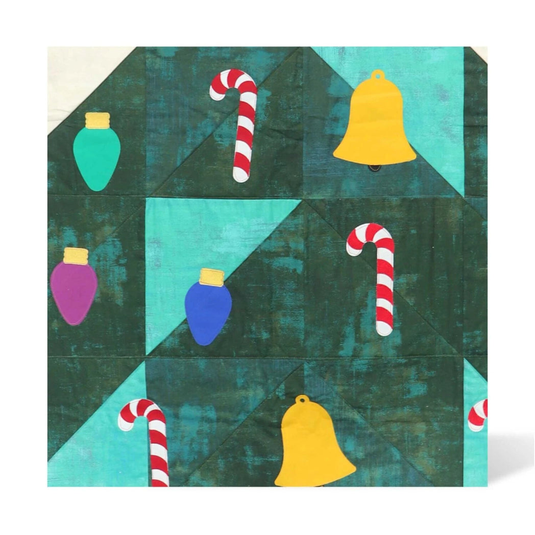 Festive quilt block in teal and dark green batik fabrics with AccuQuilt GO! Jolly Medley appliqué shapes including yellow bells, red and white candy canes, and colourful Christmas light bulbs in teal, purple and blue
