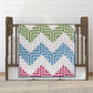 Log Cabin baby quilt draped over a wooden cot, with green, blue and pink blocks on a white background.