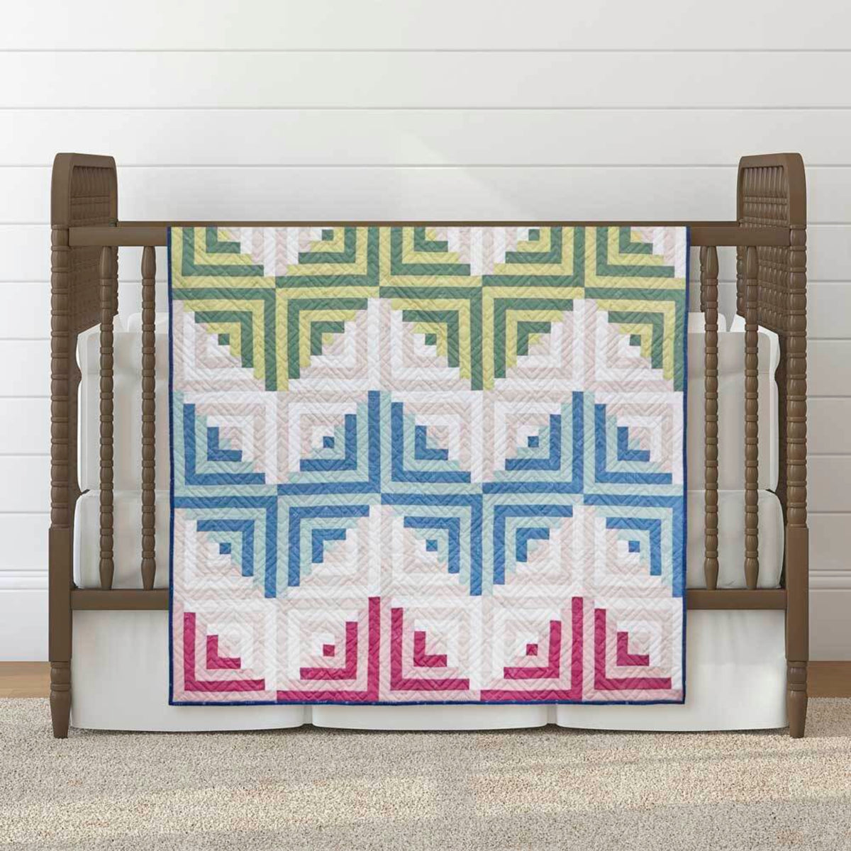 Log Cabin baby quilt draped over a wooden cot, with green, blue and pink blocks on a white background.