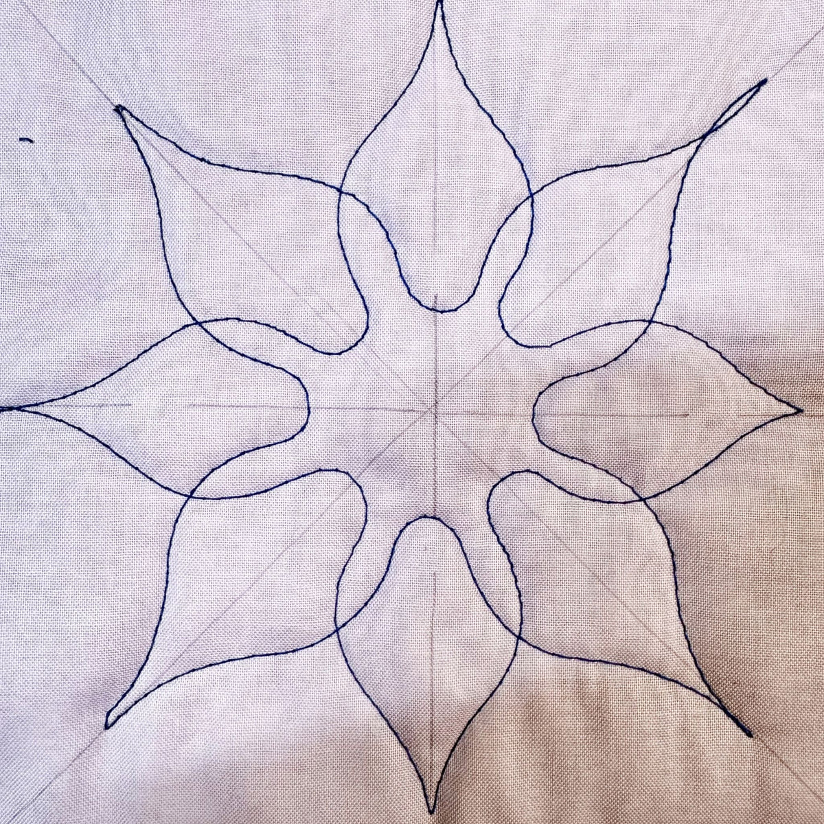 Eight-point decorative quilting motif stitched in dark thread on white fabric