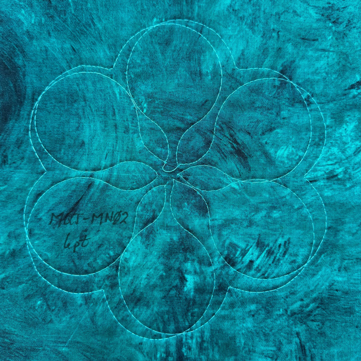 Six rounded overlapping motifs arranged in a flower-like quilting design on turquoise fabric