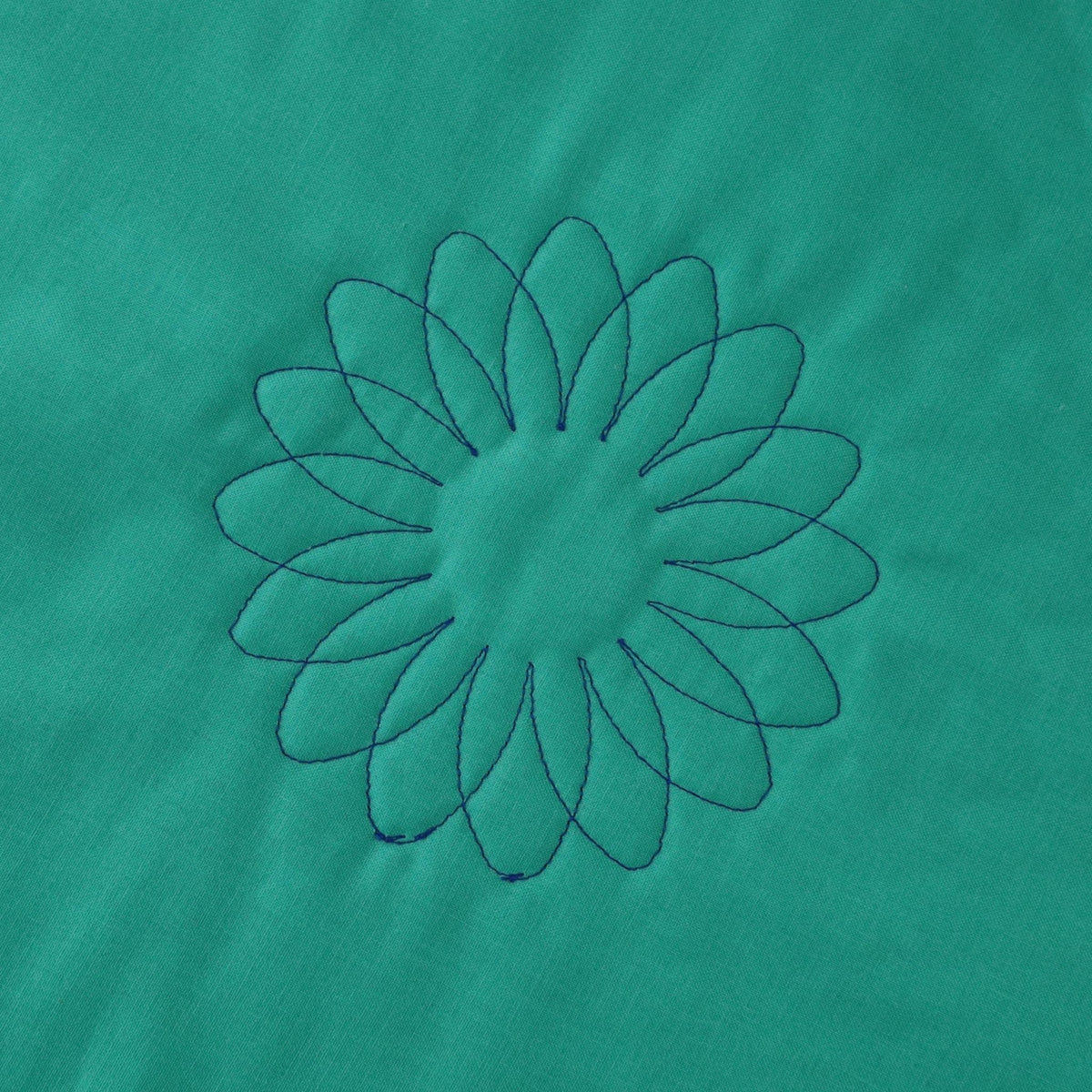 Overlapping sunflower quilting motifs forming a fuller flower in dark thread on green fabric