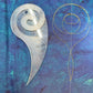 Nautilus Long Tail Feather Tool on blue fabric beside a gold-stitched spiral with an extended curved tail