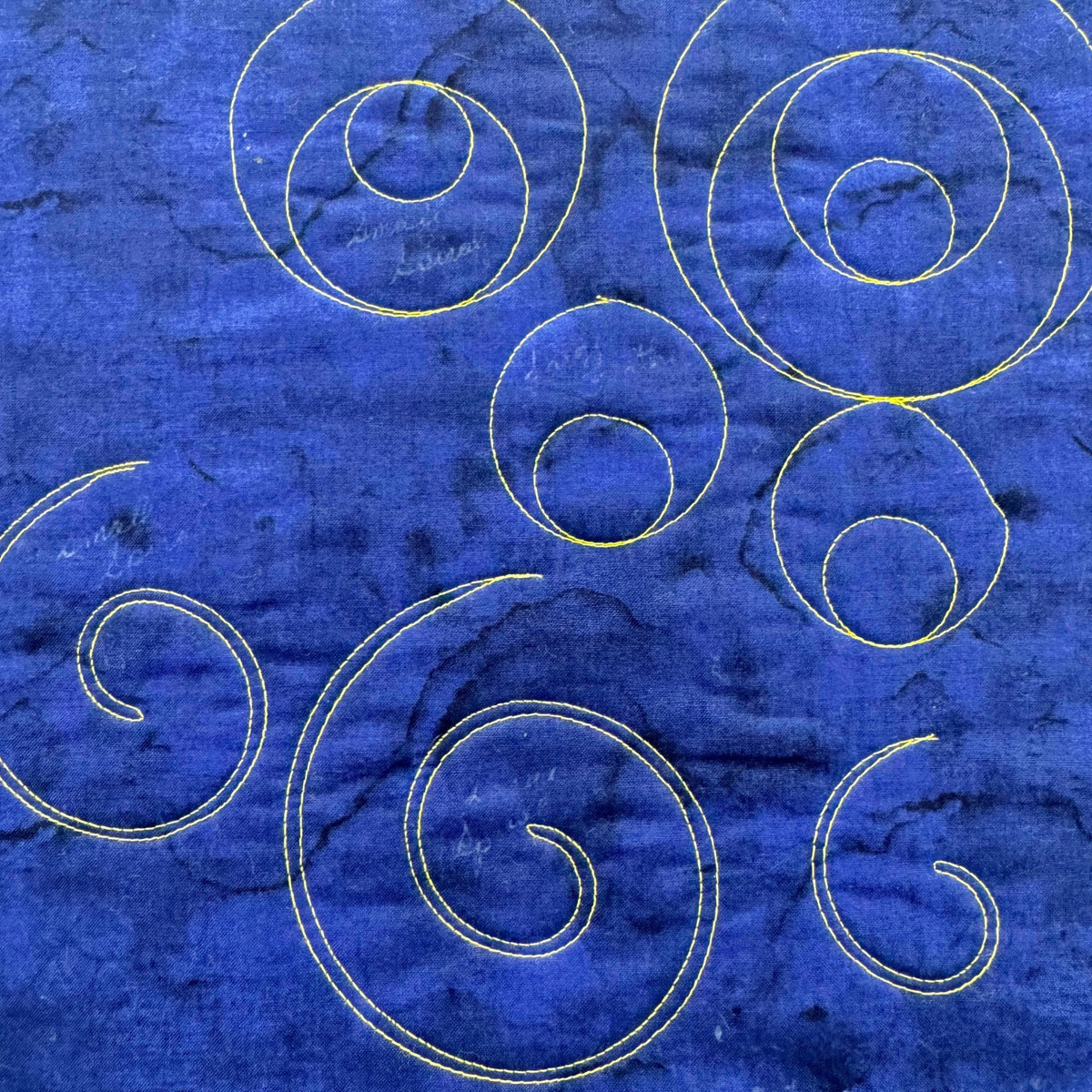 Gold-stitched quilting on blue fabric showing individual spirals in different sizes and double-line spiral designs