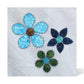 Three blue and green fabric appliqué flowers with contrasting circular centres and decorative looped stitching on white fabric, using AccuQuilt GO! Garden Variety #2 shapes.