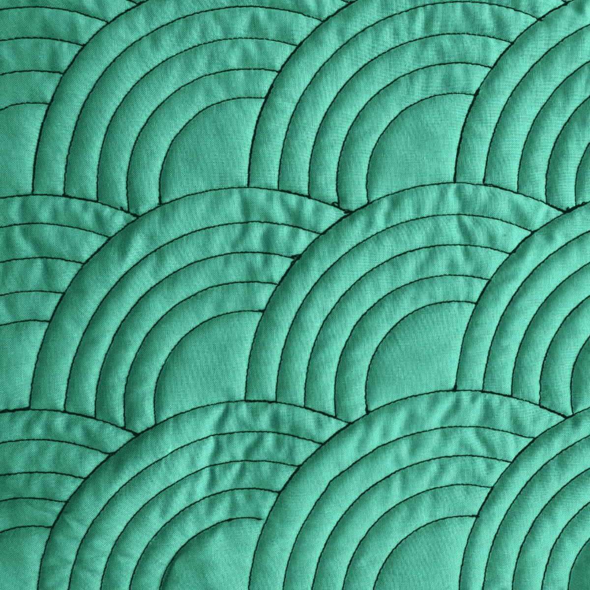 Overlapping nested arc quilting patterns with wider spacing stitched on green fabric