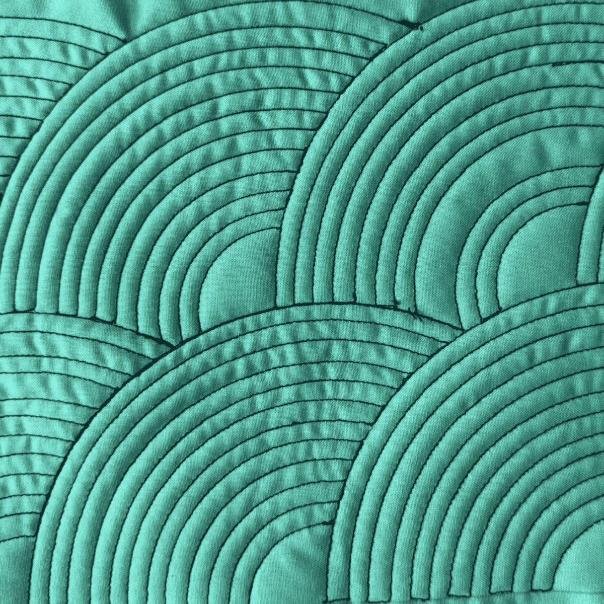 Closely spaced nested arc quilting patterns stitched on green fabric