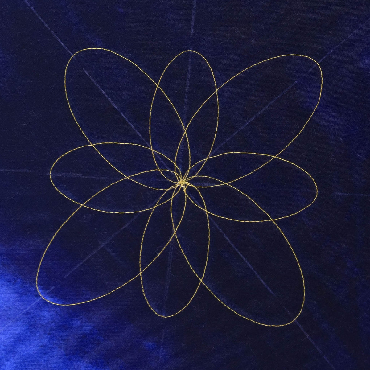 Eight overlapping oval petals forming a flower quilting design in gold-coloured thread on dark blue fabric