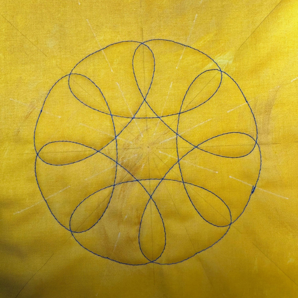Overlapping ovals arranged in a circular quilting design in dark thread on yellow fabric