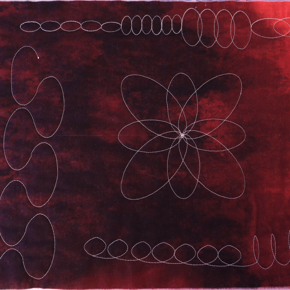 Oval chain borders and an eight-petal flower quilting design stitched in light thread on red patterned fabric
