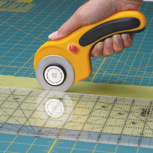 Olfa 60mm Rotary Cutter Curved Handle - In Use on a Cutting MatHand holding a yellow rotary cutter on a cutting mat