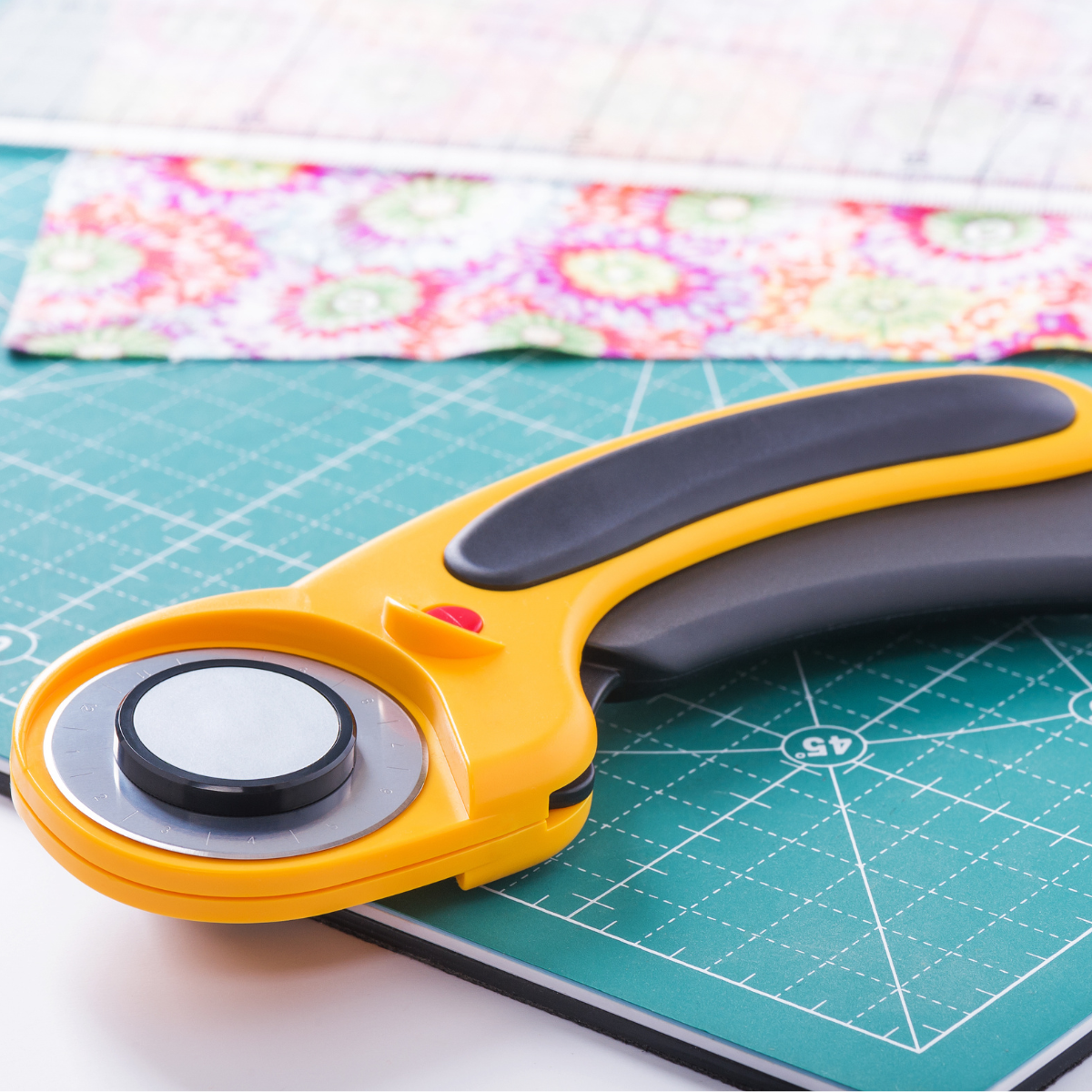 Rotary cutter on a green cutting mat with patchwork fabric — shop sewing tools at Quilt Direct

