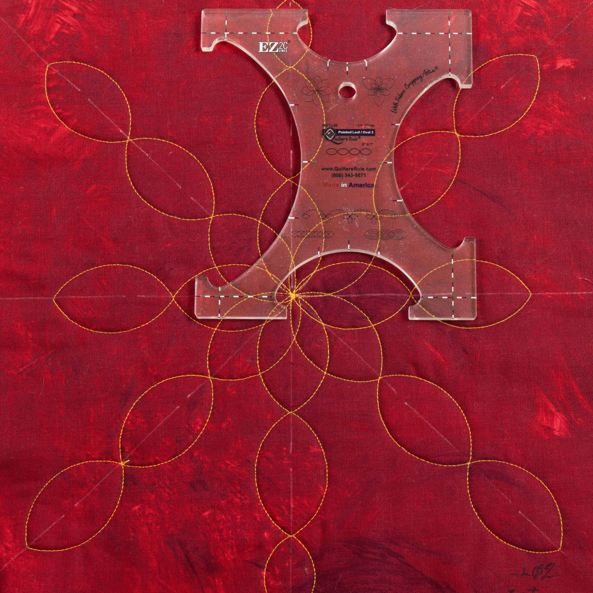 Quilter’s Rule Pointed Leaf/Oval 2 template positioned over a leaf quilting design on red fabric