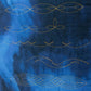 Pointed leaf chains, waves and overlapping oval quilting designs stitched in gold-coloured thread on blue fabric