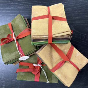 Stack of folded fabric swatches in green, brown, and beige with red ribbons on a dark surface.