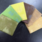 Five fabric swatches in green, yellow, brown, and beige on a dark wooden surface.
