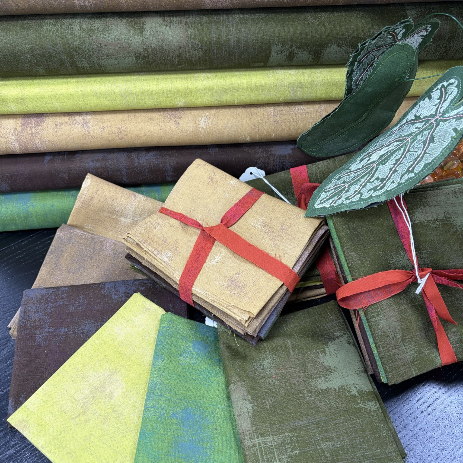 Collection of fabric swatches in various green tones with a few tied with red ribbons.