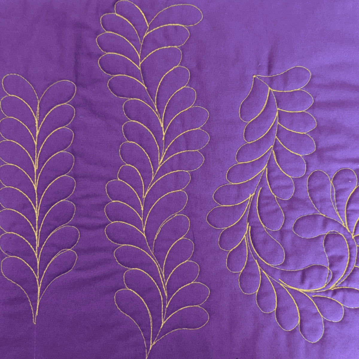 Straight and curved feather quilting designs stitched in yellow thread on purple fabric