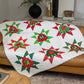 Christmas quilt made with the AccuQuilt GO! Ugly Sweater die, featuring star-bordered sweater blocks in red, green and white festive fabrics, draped over a tan leather sofa

