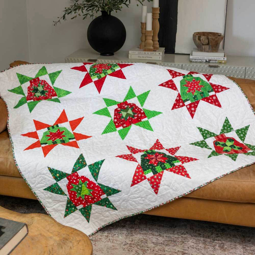 Christmas quilt made with the AccuQuilt GO! Ugly Sweater die, featuring star-bordered sweater blocks in red, green and white festive fabrics, draped over a tan leather sofa
