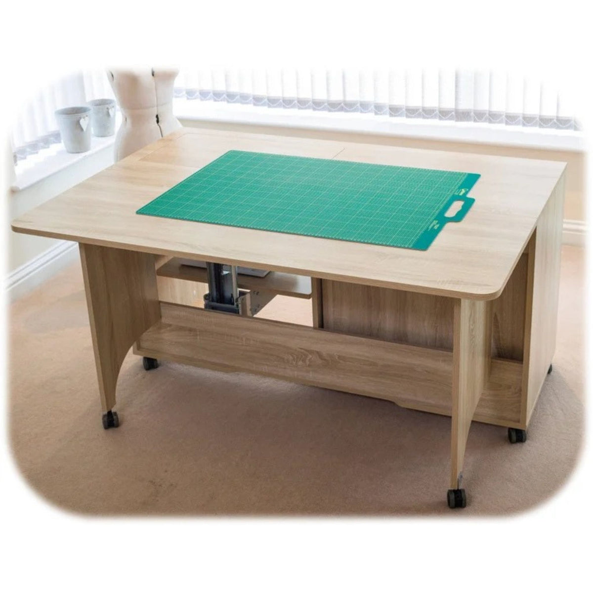 A light wood rolling craft table with a green cutting mat on top, shown in a bright room with a window and beige carpet.