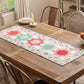 Quilted table runner on a rustic wooden dining table featuring double star blocks made with the AccuQuilt GO! Double Star die in pink, red and sage green floral fabrics on a white ditsy print background