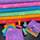 A collection of colorful 'Fat Quarter' fabric cuts arranged neatly with matching threads and decorative elements, showcasing a range of vibrant colors.